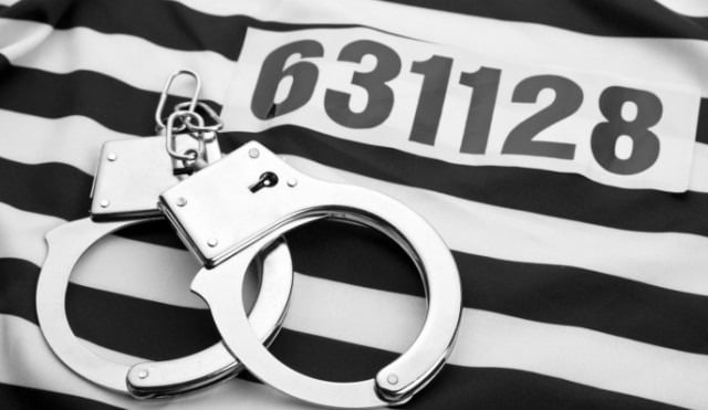 A pair of handcuffs and a sticker with a number resting on black-and-white striped fabric.