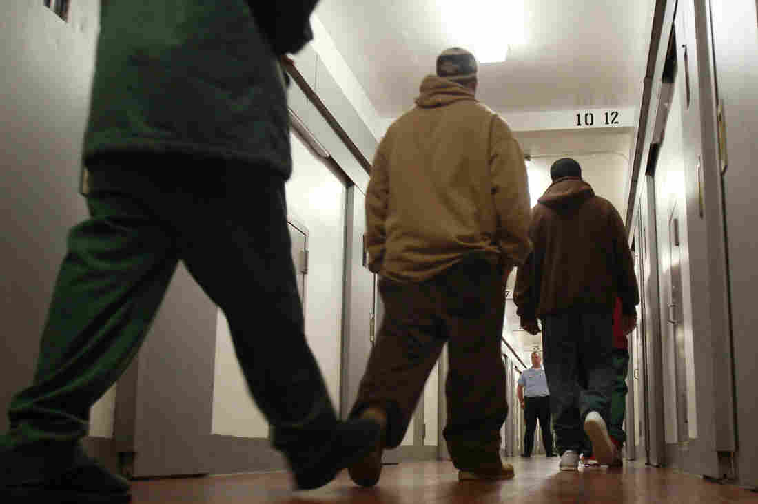Low-angle view of three men walking down a prison corridor, with a guard in the background.