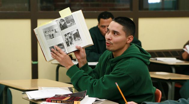 A BPI student holds up a book while speaking to the classroom.