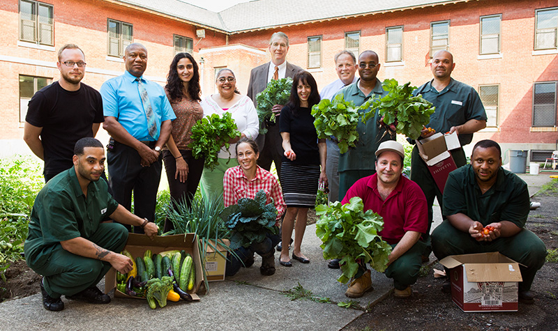 Students and staff proudly display their harvest of lettuce, cucumbers, squash and other vegetables from the garden.