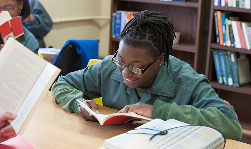 A BPI student smiles while reading a book.