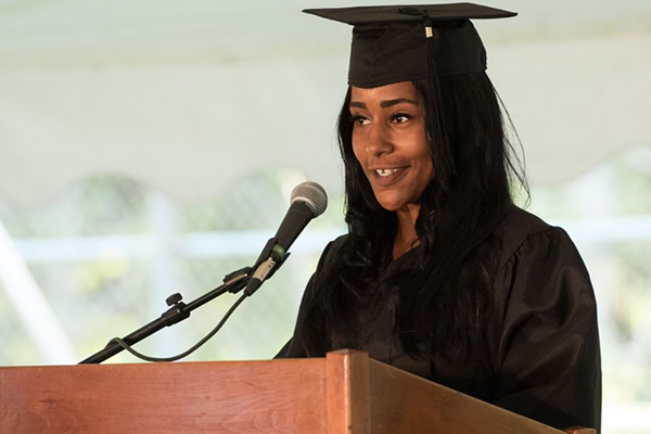 Student wearing graduation cap and gown giving a speech at a lecturn.