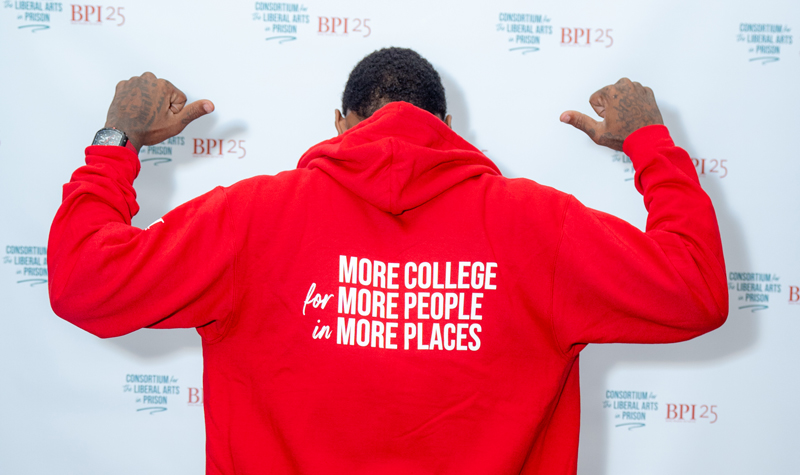 Man in a red hooded sweatshirt with the words More College for More People in More Places in white lettering.