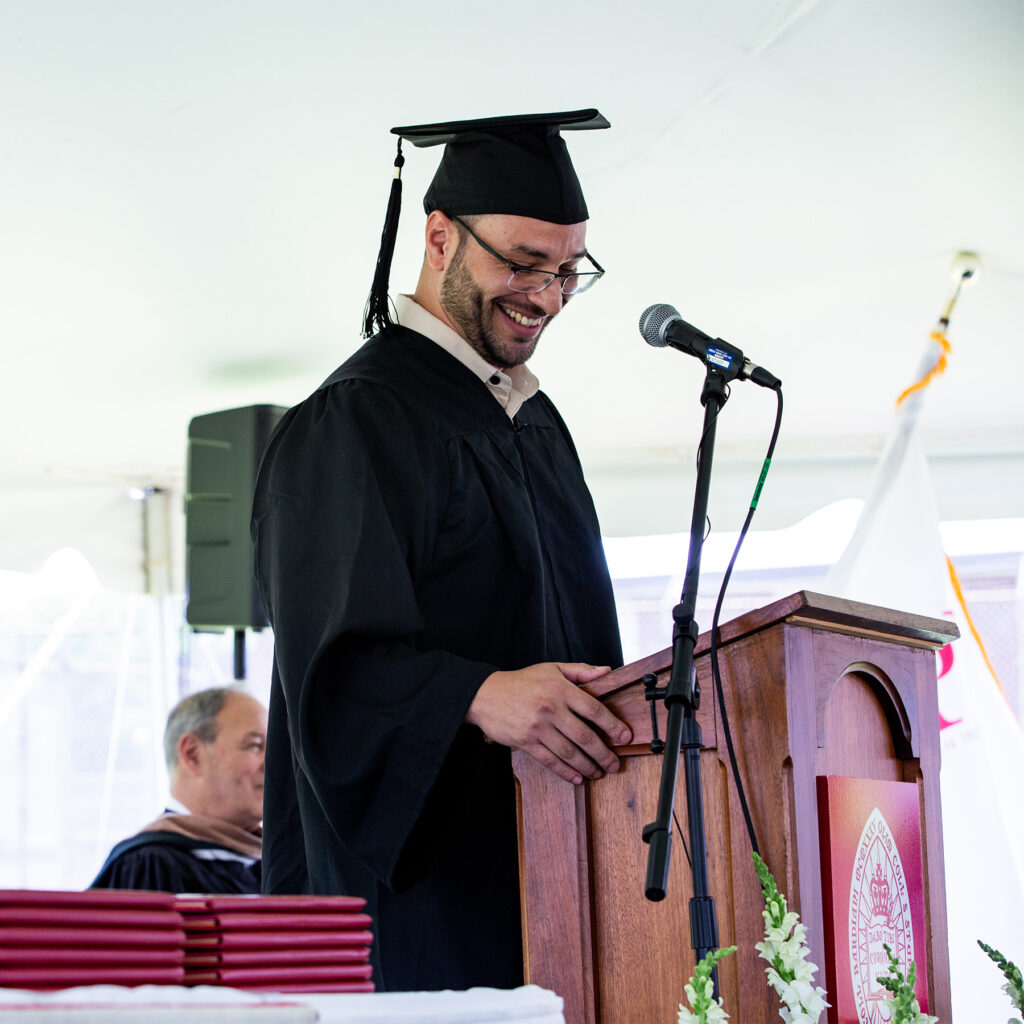 Student smiling while speaking at the podium of a BPI Commencement ceremony.