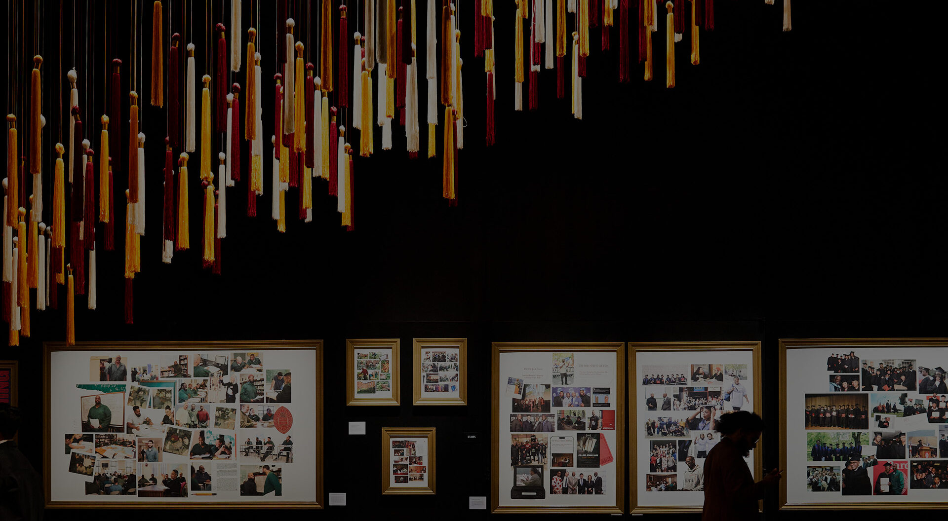 Person walking past framed collages and ceiling sculpture made of tassels at the BPI Gala 2024.