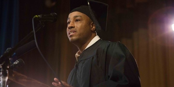 Student stands at podium wearing graduation cap and gown.